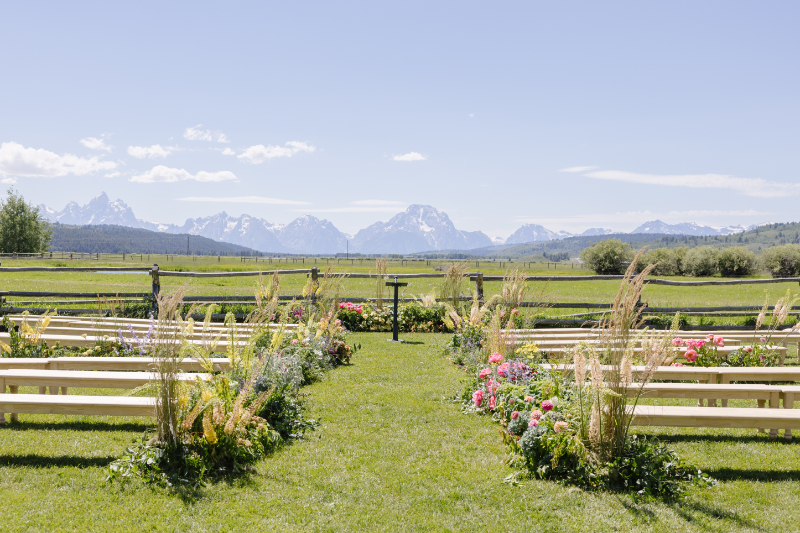 Western wedding ceremony setup in Jackson Hole with floral aisle, open ranch views, and the Grand Tetons in the background.
