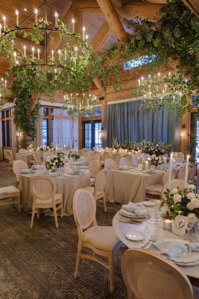 Elegant indoor wedding reception in Jackson Hole with candlelit tables, hanging greenery, and refined floral design.