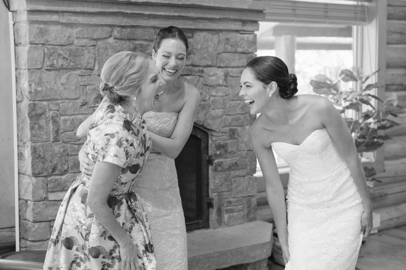 Bride sharing a joyful moment with family while getting ready at the cabin by the fireplace.