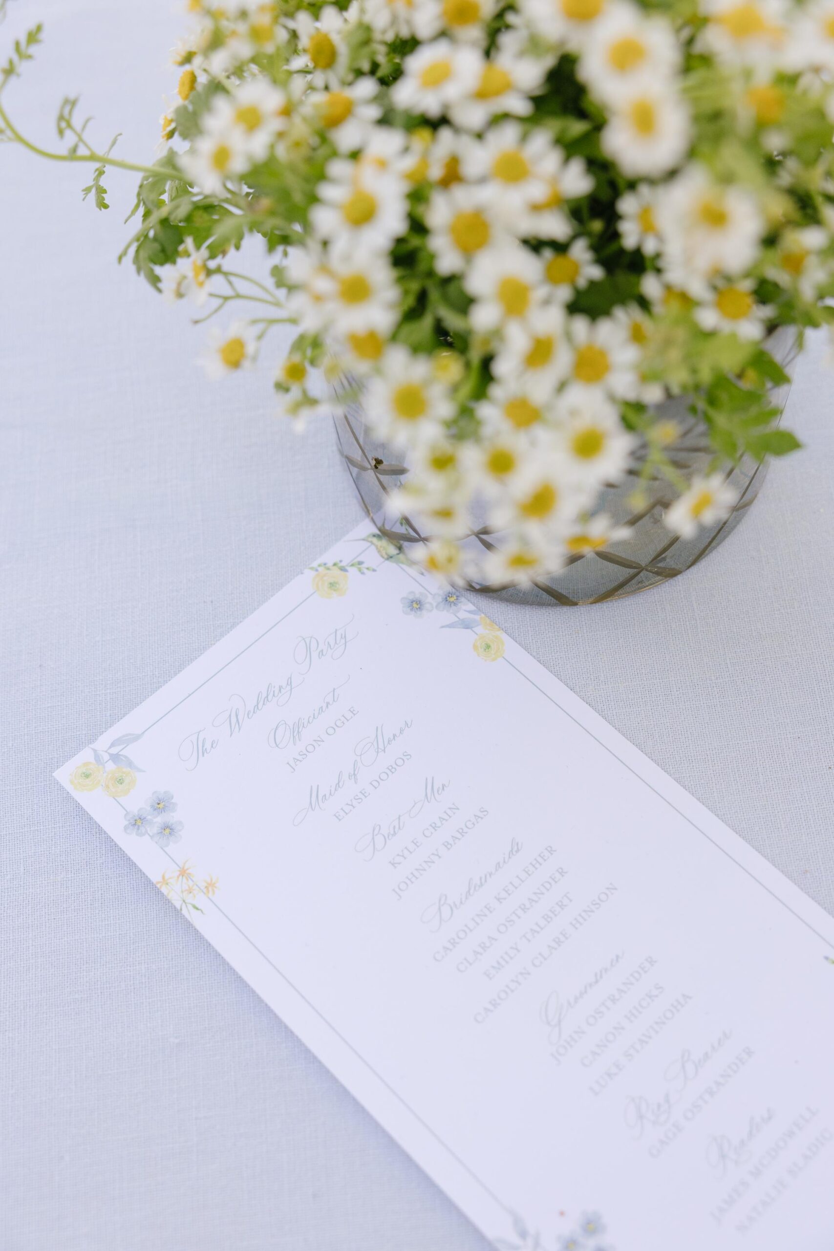 Floral wedding ceremony program with a daisy flower pot next to it.