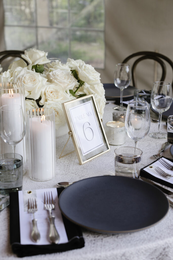 Classic wedding reception table design with white roses, candles, and black place settings
