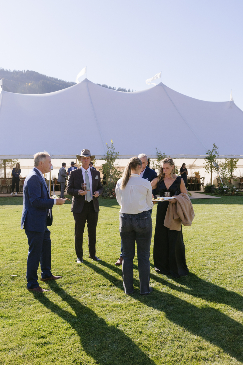 Wedding guests enjoying cocktail hour on the lawn outside the reception tent at Snake River Sporting Club