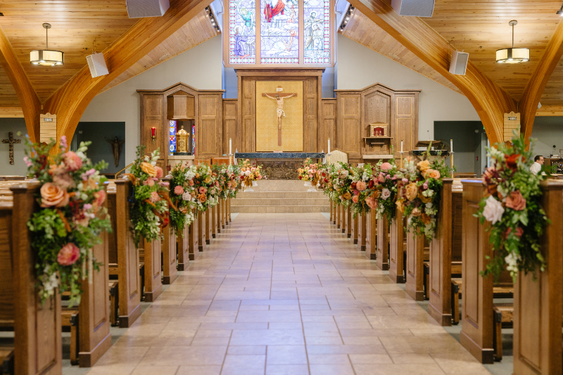 Our Lady of the Mountains Catholic Church in Jackson Hole decorated for an elegant autumn wedding, with seasonal floral arrangements lining the pews.