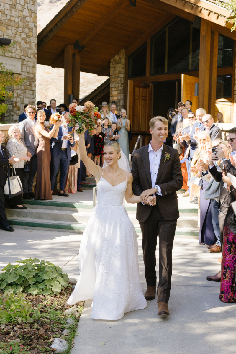 Bride lifts her bouquet in the air as her and her new husband make their grand exit after their Catholic wedding ceremony at Our Lade of the Mountains Catholic Church in Jackson Hole.