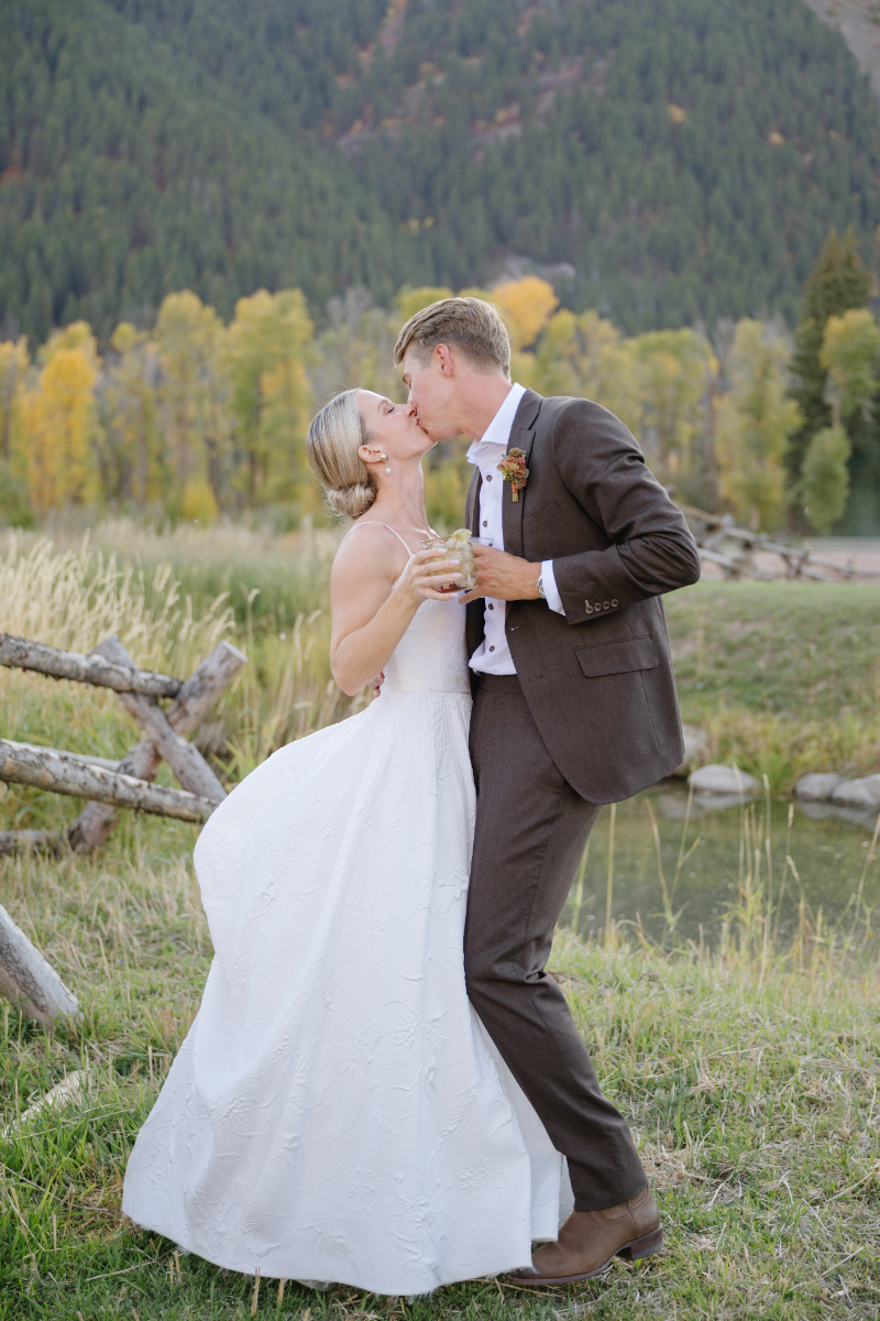 Newlyweds sharing a kiss during cocktail hour at Snake River Sporting Club with autumn mountain views