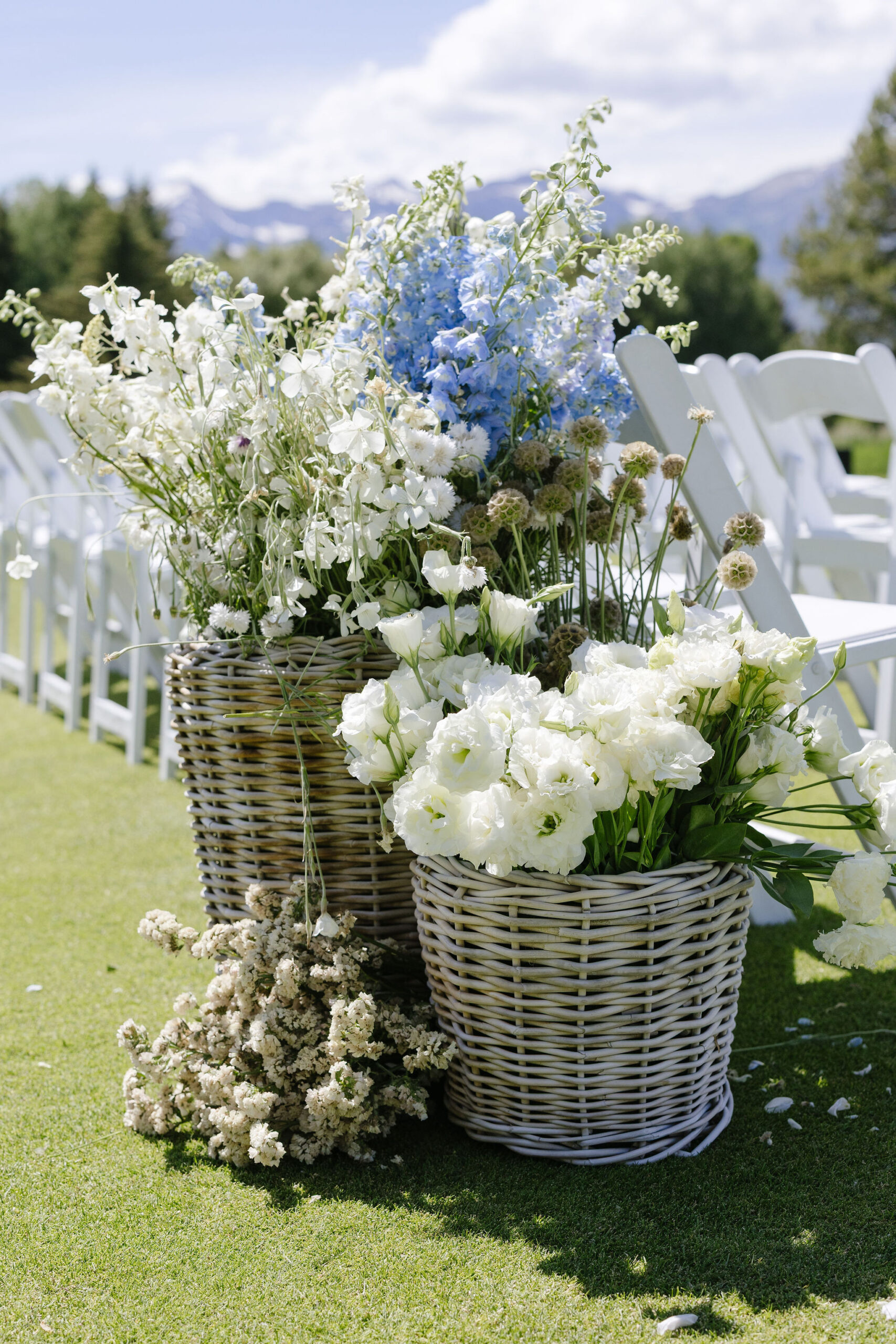Blue and white wedding flowers displayed in woven baskets at an outdoor Jackson Hole ceremony.