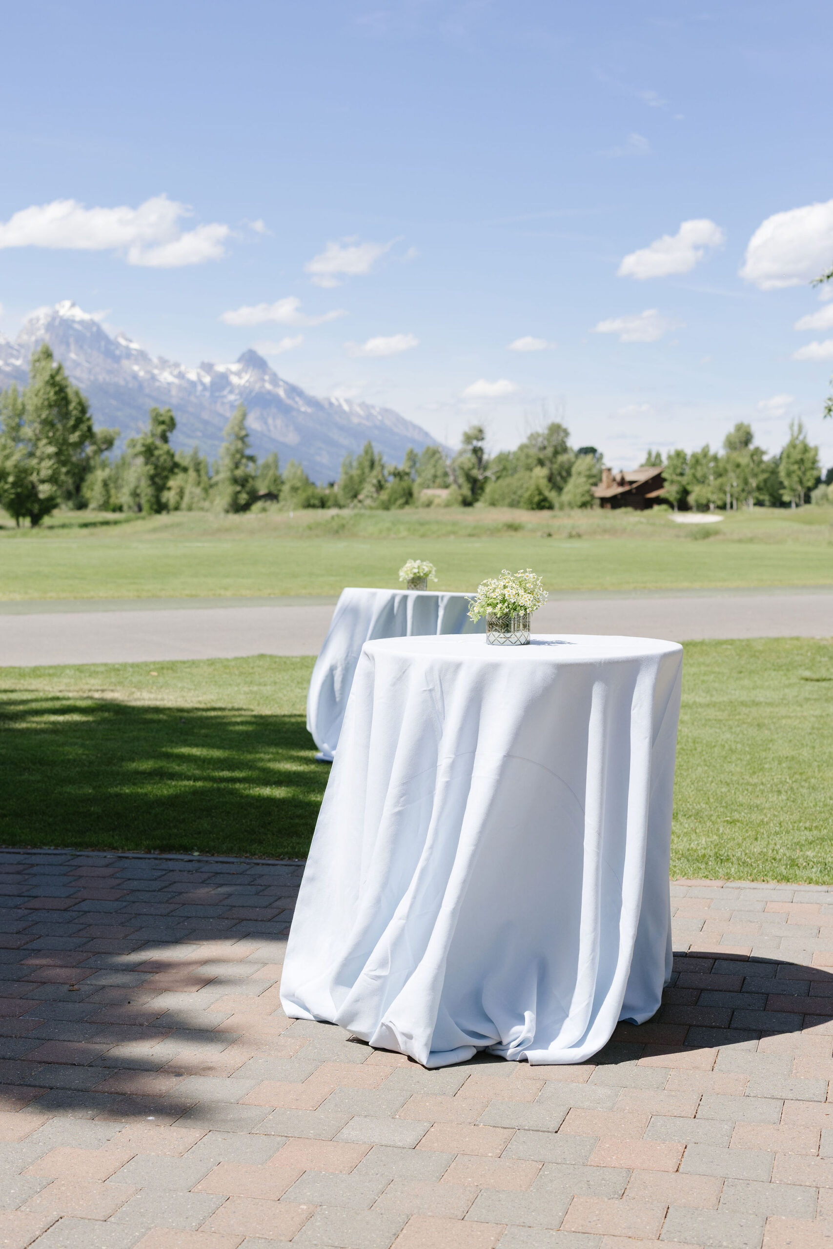 Long reception table with blue and green wedding linens, white florals, and candlelight inside a tented reception.