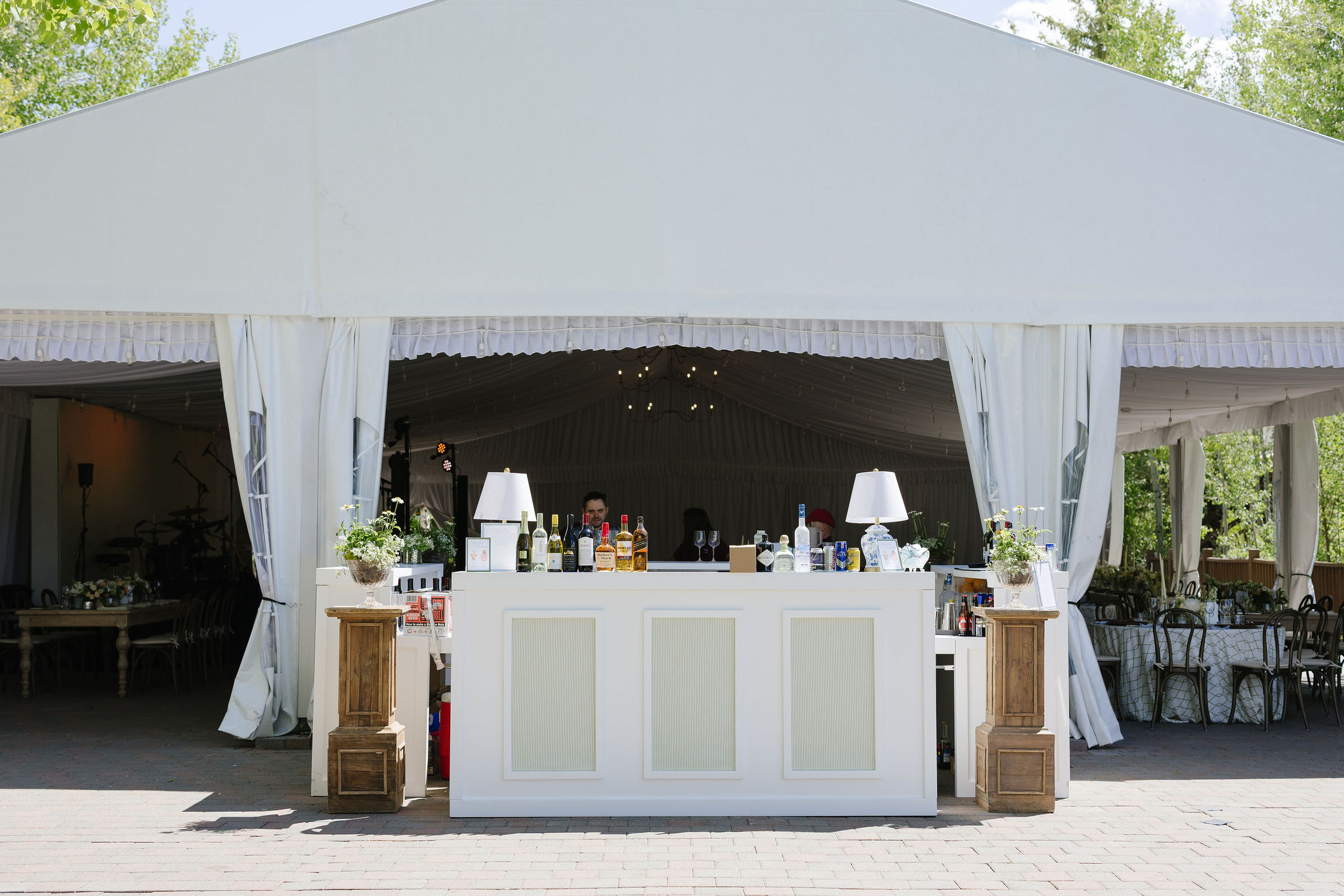 Classic white wedding bar with floral arrangements and wood accents at an outdoor Jackson Hole reception.