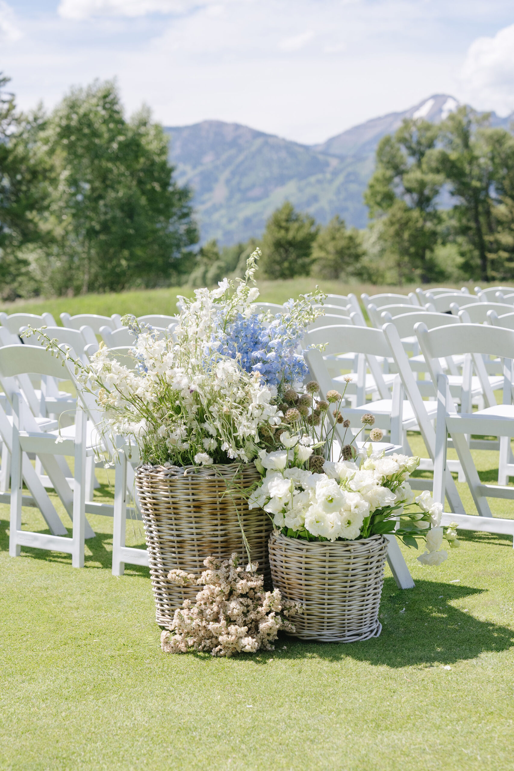 Blue and Green ceremony flowers in woven baskets with the Teton Mountains and white chairs in Jackson Hole.