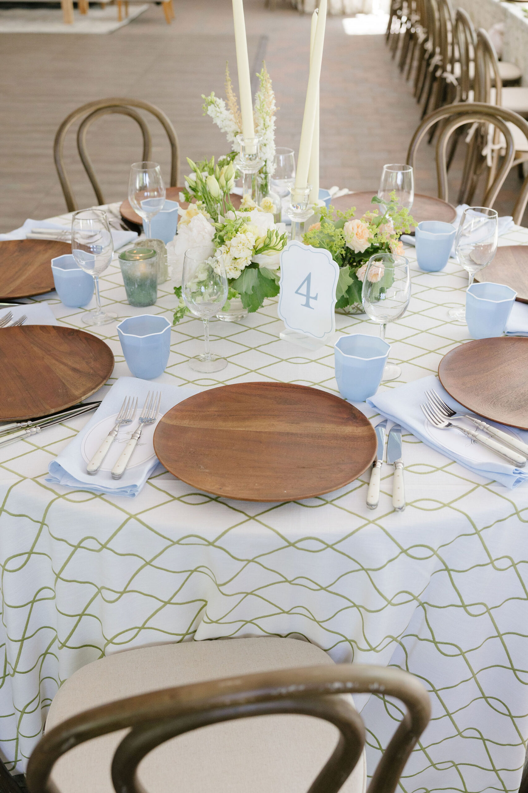 Blue and green wedding reception table with patterned linen, blue glassware, wood chargers, and garden-inspired florals.