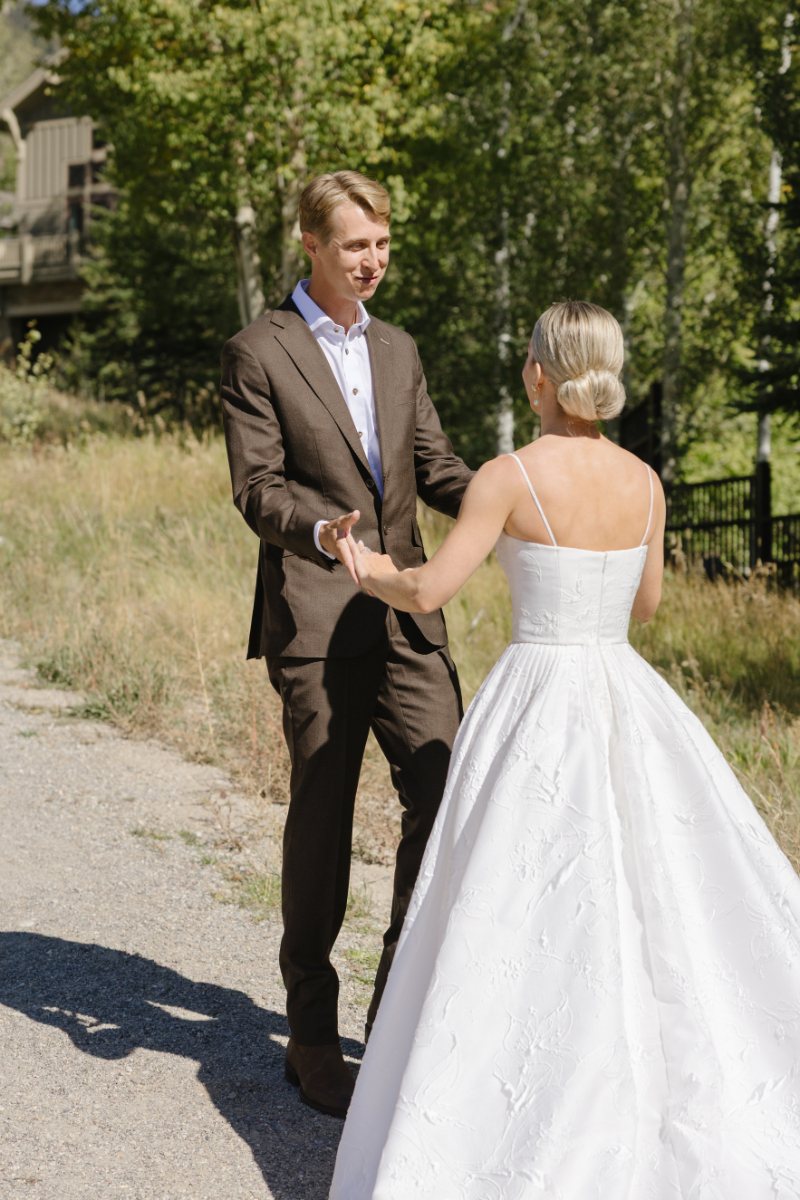 Bride and groom holding hands and smiling as they look at each other lovingly during their first look.