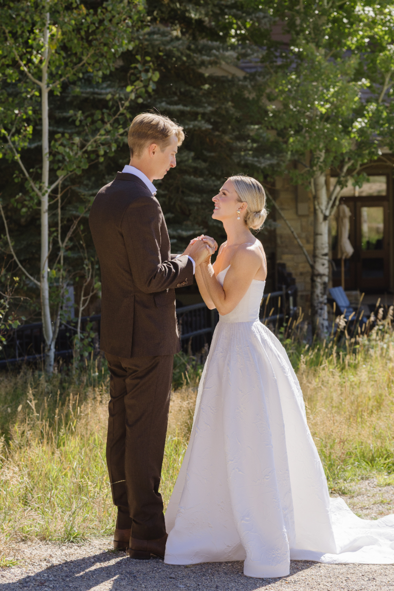 Bride and groom holding hands and smiling as they look at each other lovingly during their first look.
