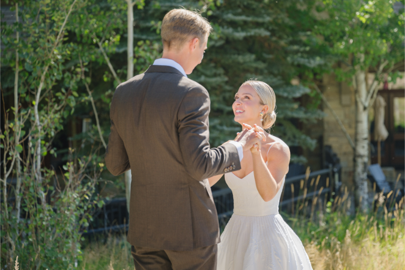 Bride and groom holding hands and smiling together as they look at each other lovingly during their first look.