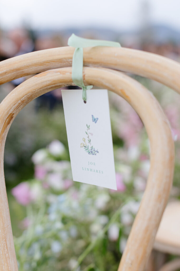 Wedding ceremony ideas with a personalized escort card tied to a wooden ceremony chair with floral details.