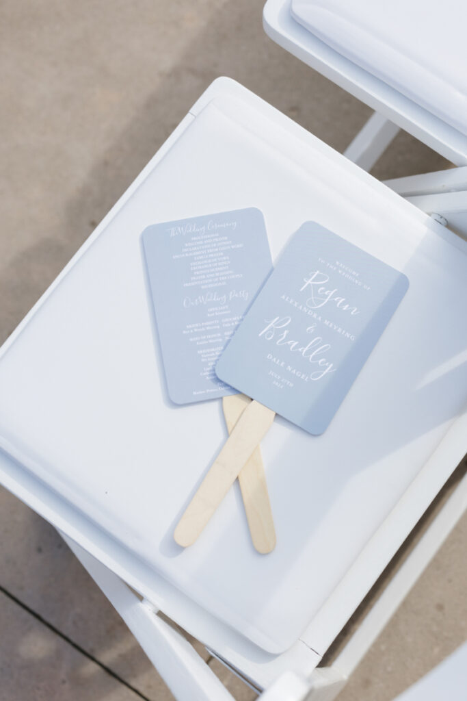 Blue Jackson Hole wedding ceremony program fans displayed on white chairs