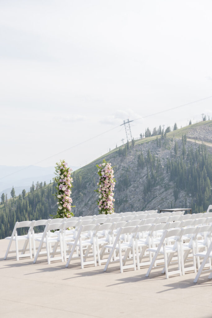 Mountain wedding ceremony with white chairs and pastel floral columns