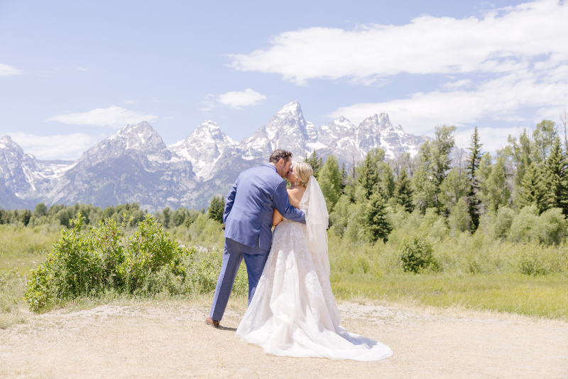 Natural wedding picture pose of a bride and groom kissing with the Grand Tetons behind them