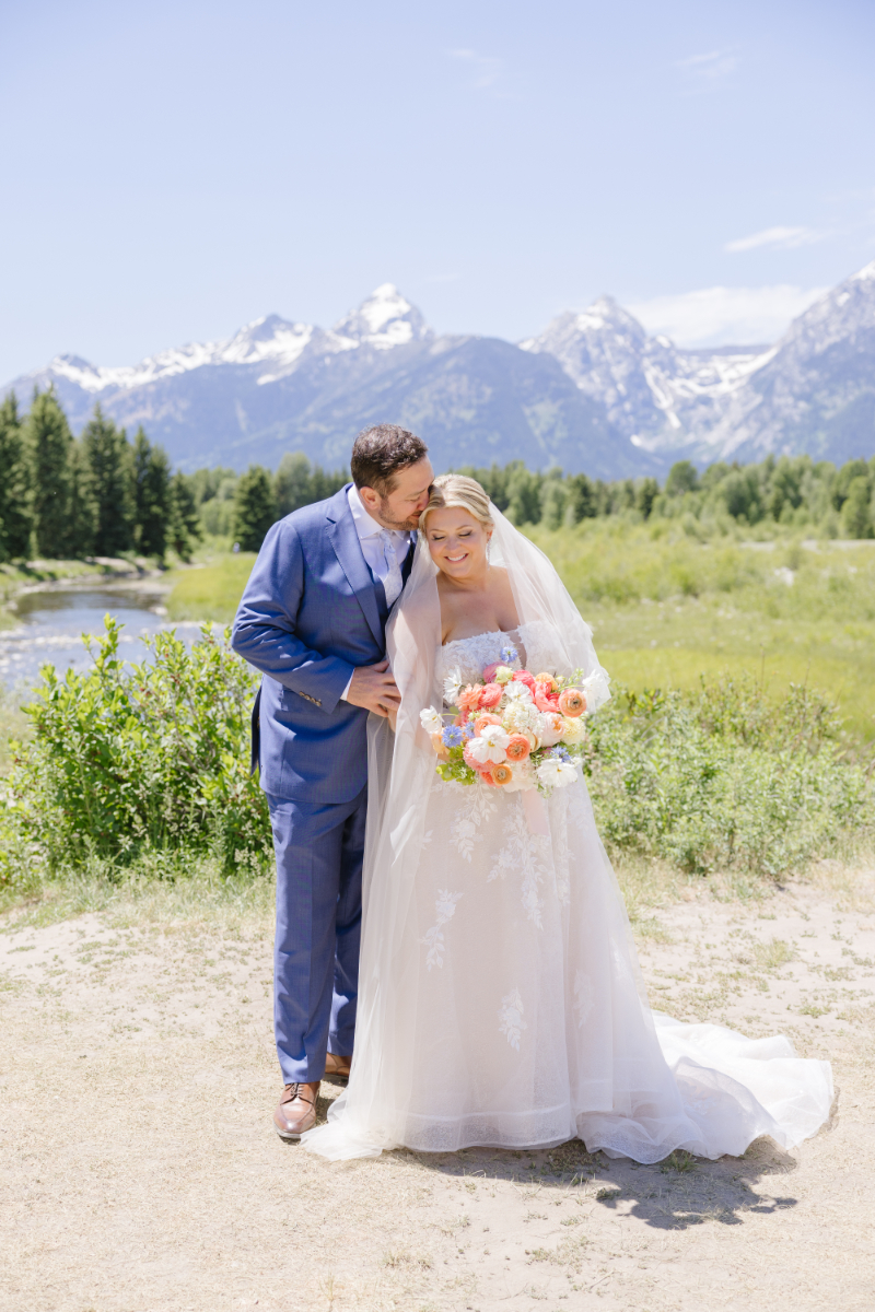 Natural wedding picture pose of a bride and groom embracing with the Grand Tetons in the background