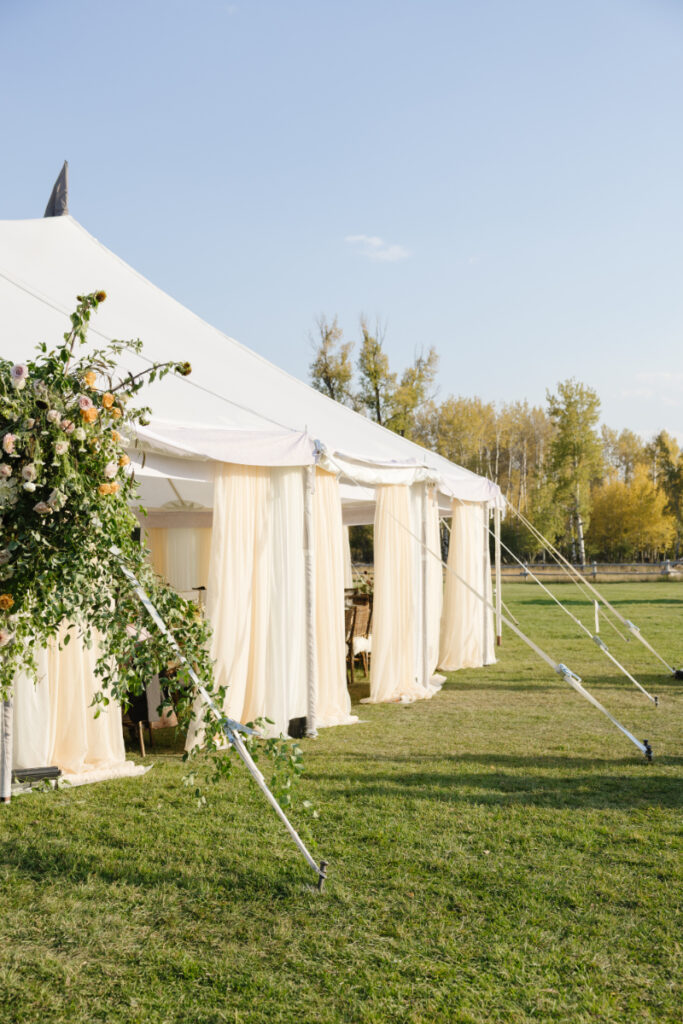 Elegant sailcloth wedding tent with flowing drapery and floral accents on a Jackson Hole wedding venue lawn.