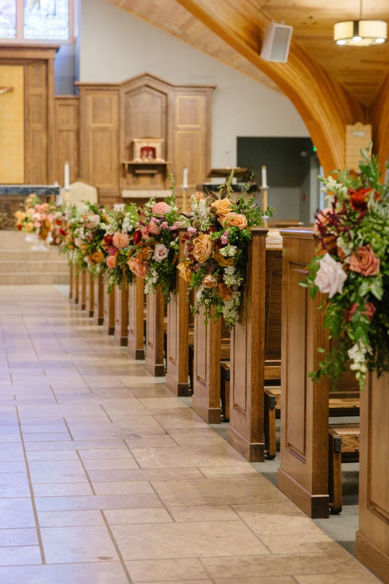 Church wedding aisle lined with colorful floral arrangements decorating the pews before a Jackson Hole wedding ceremony.
