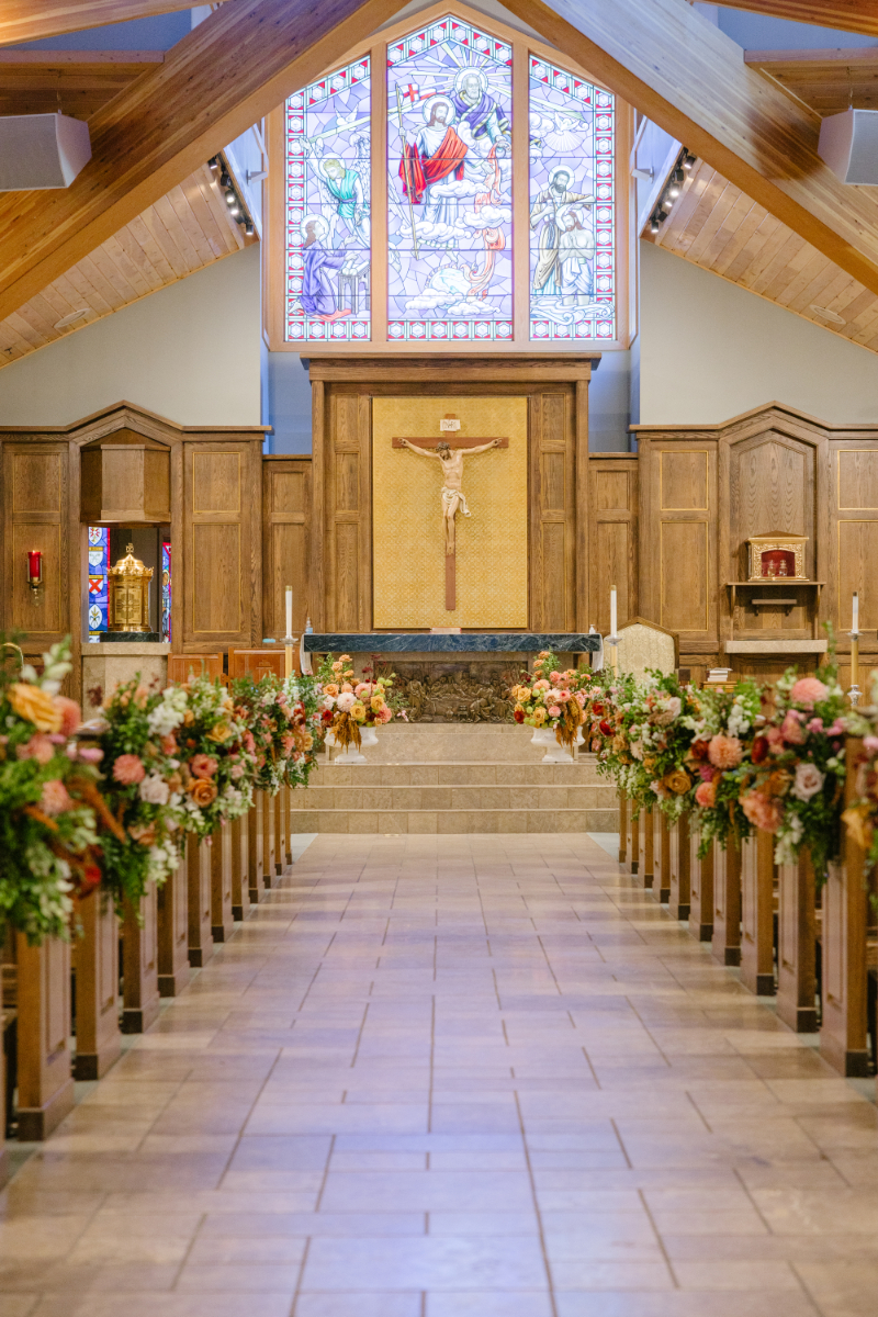 Floral-lined church aisle leading to the altar beneath stained glass windows during a Jackson Hole wedding ceremony.