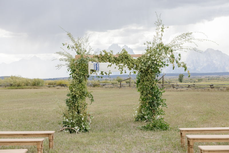 Outdoor wedding ceremony arch with lush greenery and the Teton Mountains in the background at a Jackson Hole wedding venue.