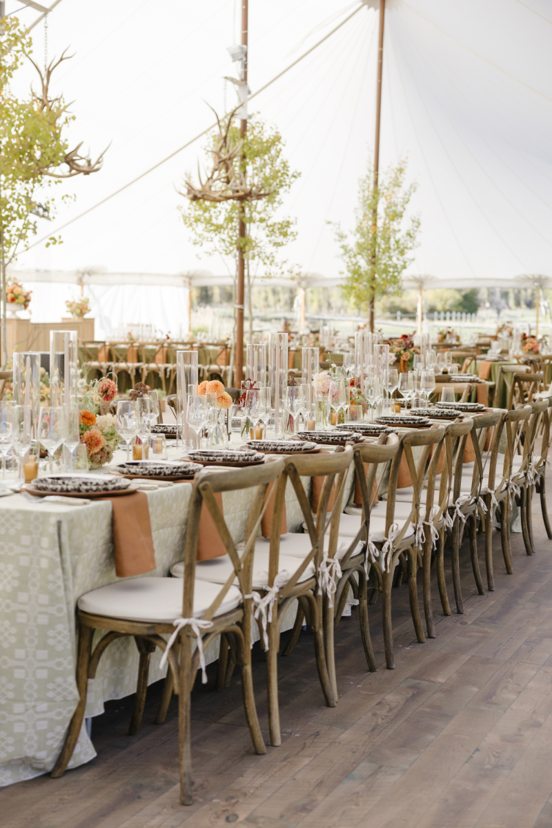 Elegant wedding reception tables inside a white tent with colorful florals and rustic wood chairs
