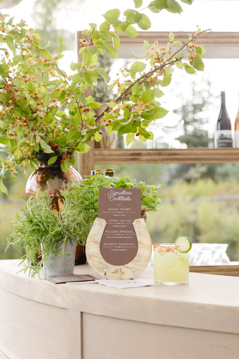 Signature cocktail bar decorated with fresh greenery and berry branches at a Jackson Hole wedding