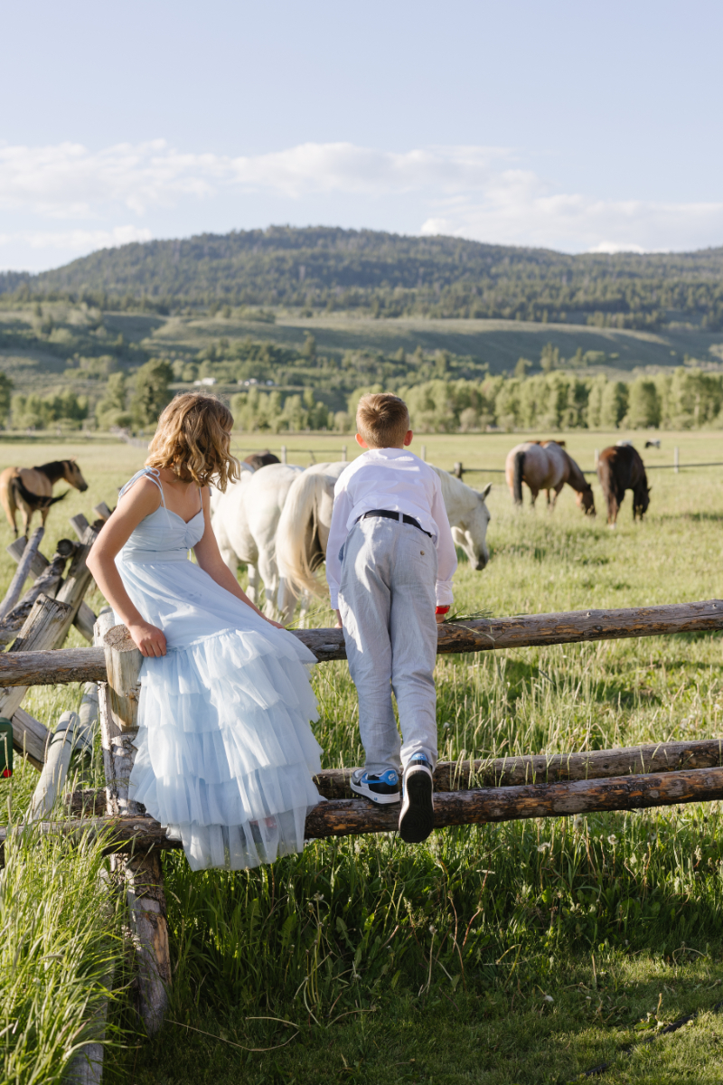 Young wedding guests watching horses from a rustic wooden fence during a Jackson Hole celebration